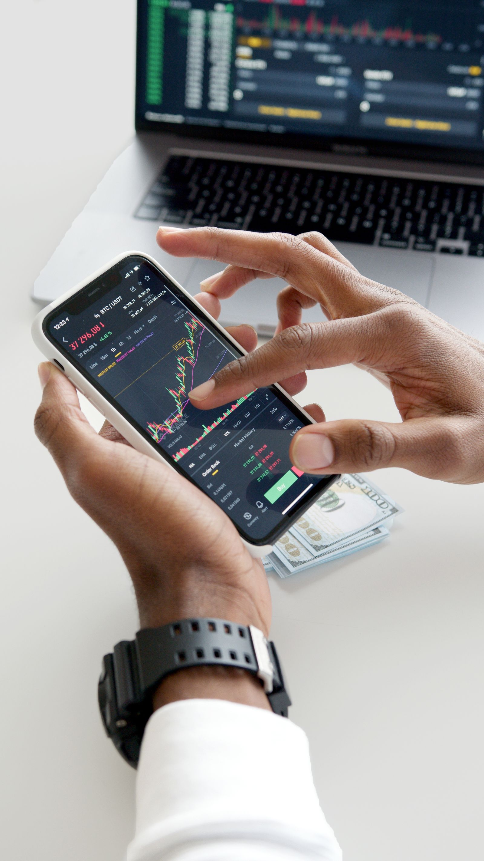 Hands using a smartphone trading app with charts and dollar bills in the background