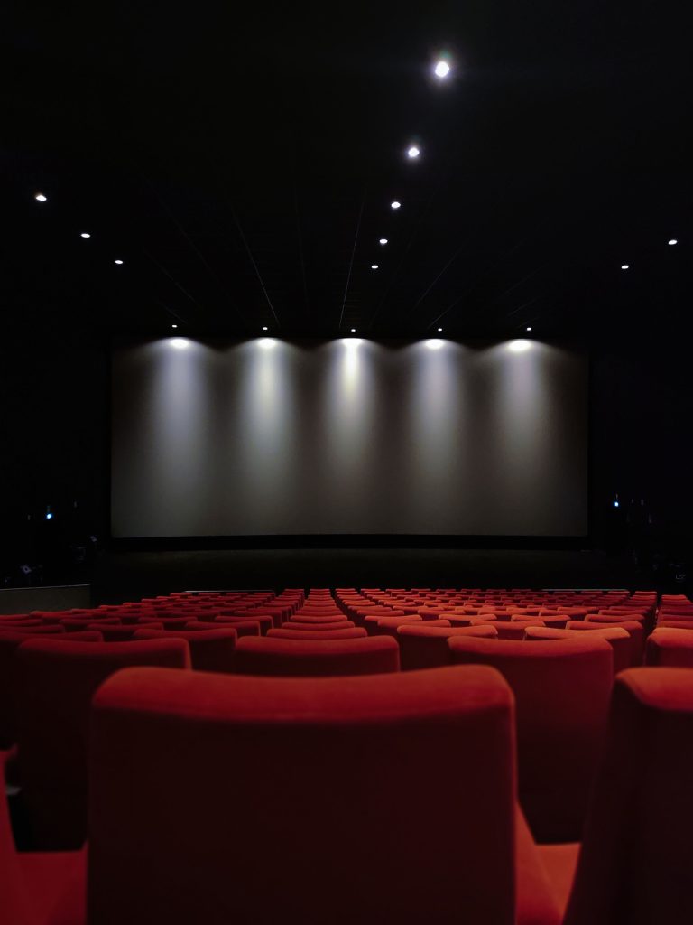 An empty cinema with rows of red seats facing an illuminated screen