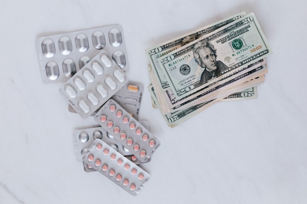 Medication packaging resting on a stack of U.S. dollar bills, illustrating medical costs.