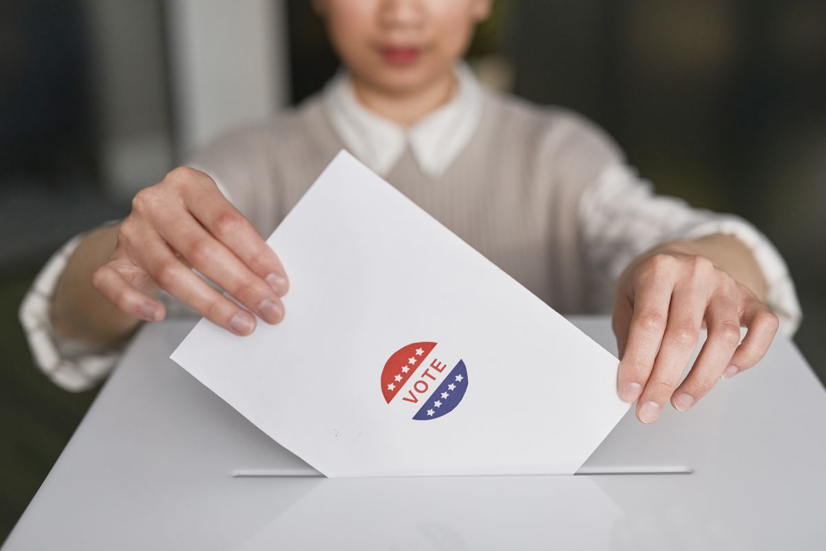 Close up of a hand placing a paper ballot into a voting box