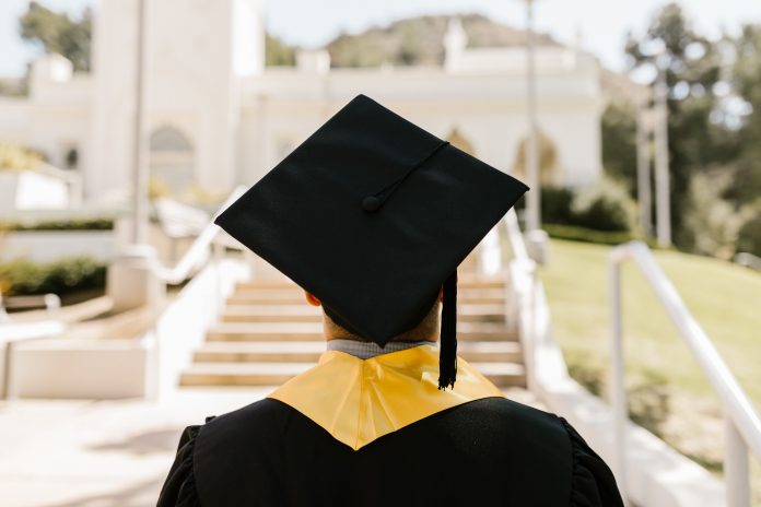 A college graduate in cap and gown standing outdoors.
