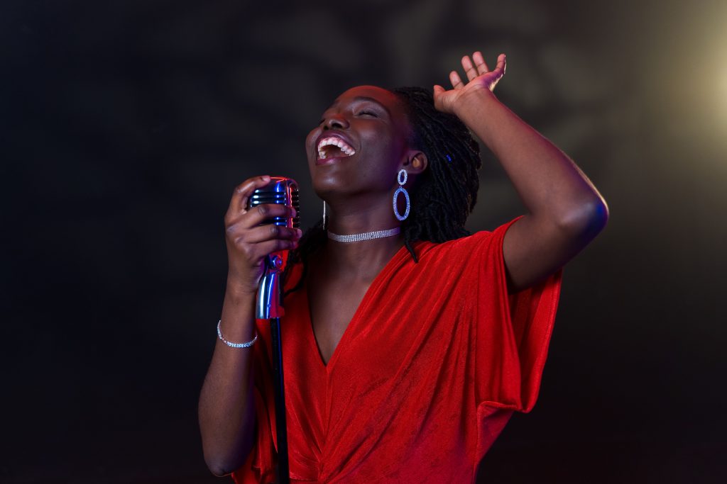 A Black woman singer performing on stage with a microphone under warm lighting
