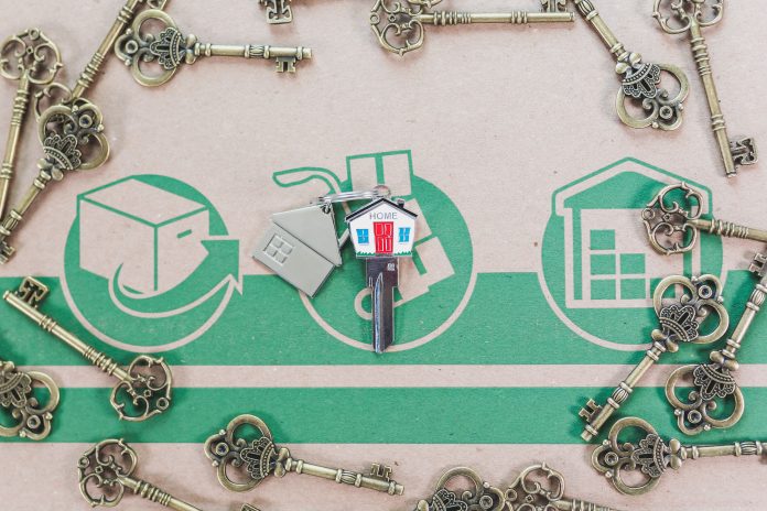 A hand holding house keys in front of a home, representing the Black homeownership and appraisal gap
