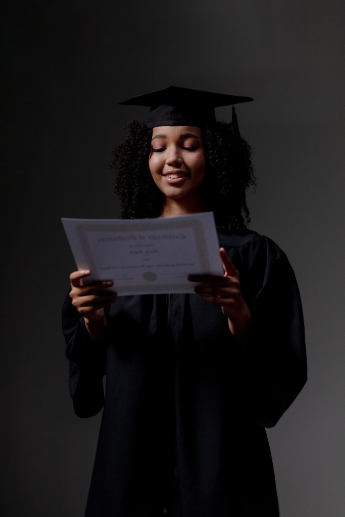 A Black graduate in cap and gown holding a diploma, representing HBCU history and achievement